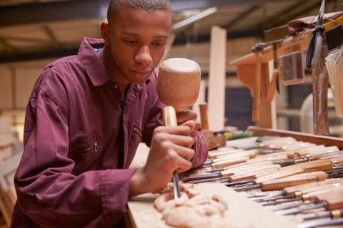 Apprentice Using Chisel To Carve Wood In Workshop Foto stock