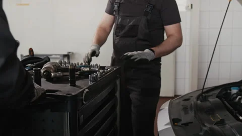 Apprentice Wheeling Tool Cart to Chief Mechanic Working on Car in Garage Stock Footage 329410416