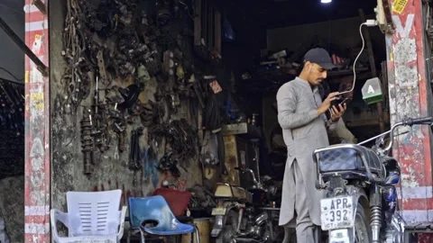 An apprentice worker is seen at the workshop using a cellphone while it is Stock Footage 300651387