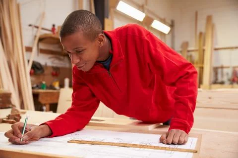 Apprentice Working With Plans In Carpentry Workshop 스톡 사진
