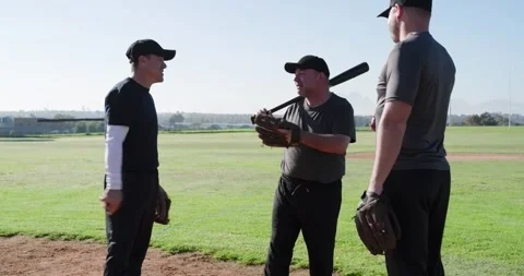 Approaching coach carrying bat teaching swing to two male players on baseball 動画素材 341664515