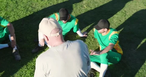 Approaching, Diverse baseball coach guiding players in jerseys on outfield grass Stock Footage 340964112
