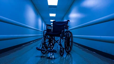 Approaching an empty wheelchair sitting in an empty hospital corridor Stock Footage 120307447