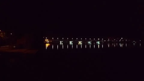 Approaching a lighted bridge in complete darkness over water Video stock 135438799