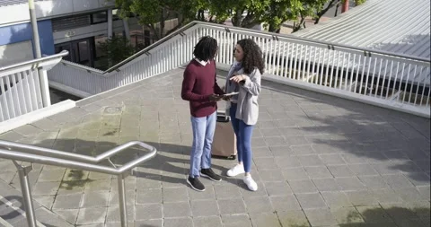 Approaching ramp top, Diverse couple scrolling tablet and pulling suitcase to Stock Footage 337537081