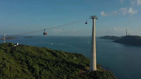 Approaching two cable cars in sunset above mountain with green trees and sea wa Stock Footage 124367056