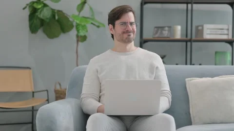 Approval Gesture by Young Man Using Laptop while Sitting on Sofa Stockbeeldmateriaal 286163051