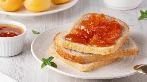 Apricot jam on bread in a white plate and a jar of apricot jam Stock Footage 283178629