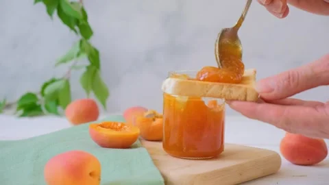 Apricot jam in a jar. A woman's hand spreads apricot jam on toast. Stock Footage 285220341
