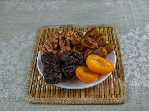 Apricots, prunes, dates, walnuts on a white saucer standing on a bamboo napkin. Stock Photos