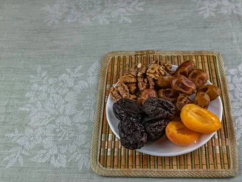 Apricots, prunes, dates, walnuts on a white saucer standing on a bamboo napkin. Stock-Fotos