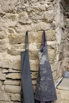 Aprons hanging on a stone wall in a workshop on a bright day Stock Photos