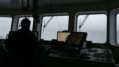 Aptain stands silhouetted inside bridge of a small vessel in a storm 스톡 동영상 135964315