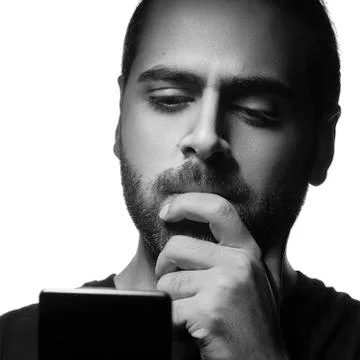 Arab guy using a smartphone and thinking. Black and white head shot of bearde Foto stock
