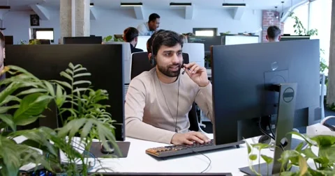 Arab handsome man in headset working at computer screen and talking with client Stock Footage 179985143