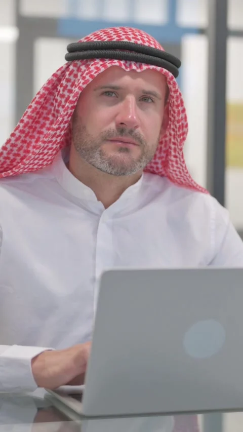 Arab Man Looking at Camera while Working on Laptop in Office, vertical video Stock Footage 324777253