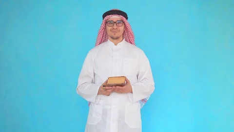 Arab man with a rosary and a book in his hands stands on a blue background Video stock 106989636