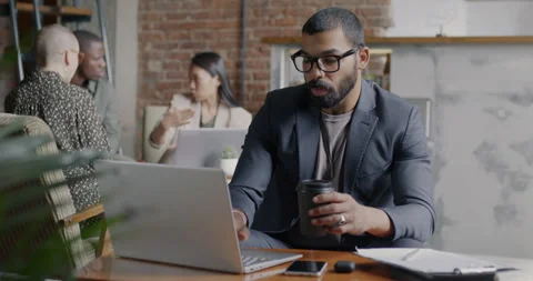 Arab man in suit using laptop and drinking coffee sitting at table in creative Stock Footage 249058588