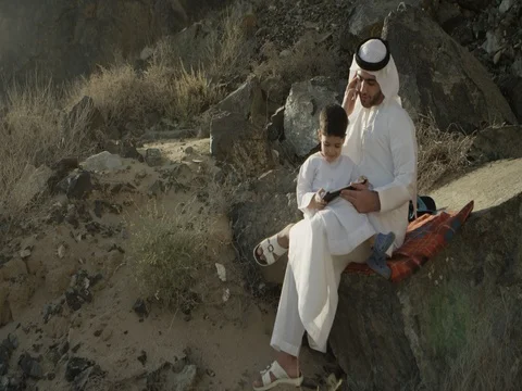 Arab man talking on mobile while son using digital tablet. Stock Footage 69459197