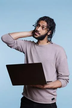 Arab programmer holding laptop, uncertain about software app development Foto stock