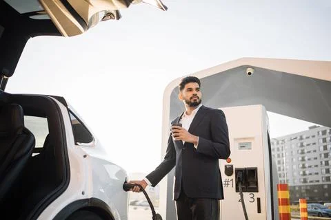 Arabian man drinking coffee while charging car 스톡 사진