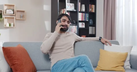 Arabian young man calling and talking on smartphone at home. Handsome male Stock Footage 179946147