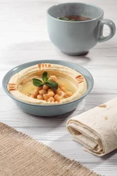 Arabic breakfast Hummus dish with bread and cup of hot mint tea on wooden whi Stock Photos