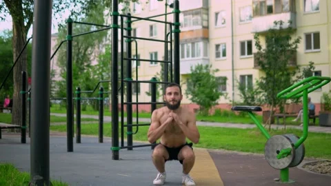 Arabic man with a beard without sportswear makes squats on a public platform. Stock Footage 200845017