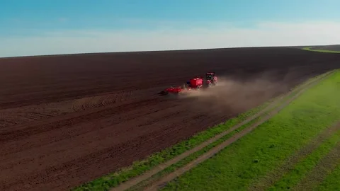 Arable, red tractor plough furrows the ground and moves forward, behind it rises Stock Footage 149303435