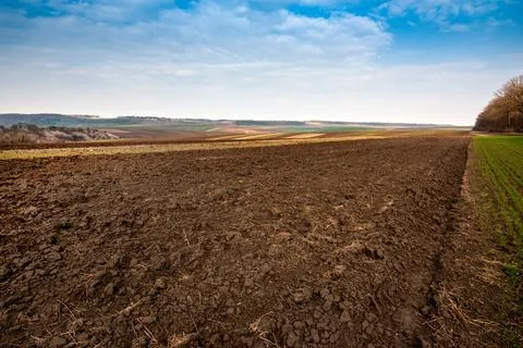 Arable spring field, plowed soil and relief hilly, landscape in the backgroun Stock Photos