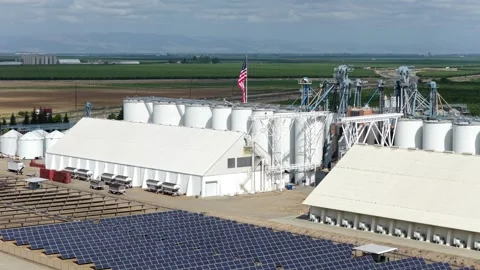 Arbuckle almond processing facility towers above neat solar panel rows Stock Footage 337694179