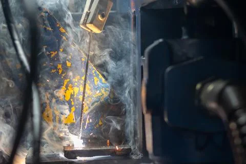 An arc welding process generates bright light and smoke on steel components. Fotos Stock