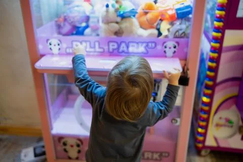 Arcade claw machine filled with plush toys being explored by a young child Stock Photos