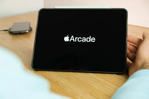 Arcade logo on the screen of the IPad tablet with charging smart phone on the Stock Photos
