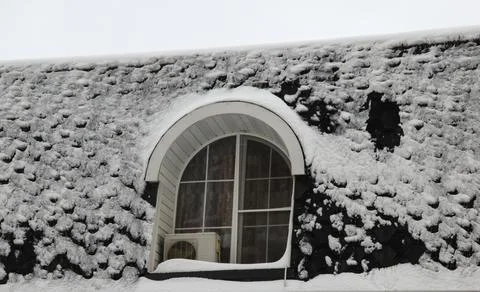 An arch-shaped window covered the wall and the roof with snow. Stock Photos