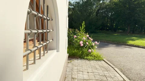 Arched barred window stands quietly next to a sunlit park path Stock Footage 336877202