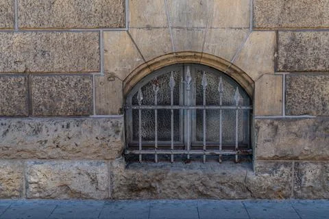 Arched basement window in a stone wall with beautiful wrought iron bars Stock Photos