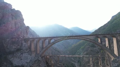 Arched bridge stands in mountain landscape with rocky terrain and green hills Stock Footage 342706010