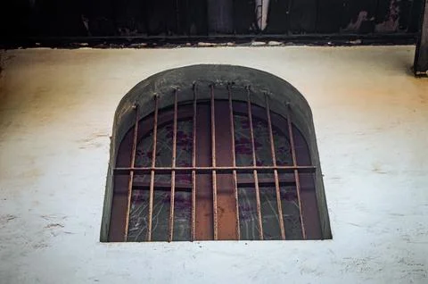 An arched, rustic window with rusty bars and a glimpse of dark, potentially.. Stock Photos