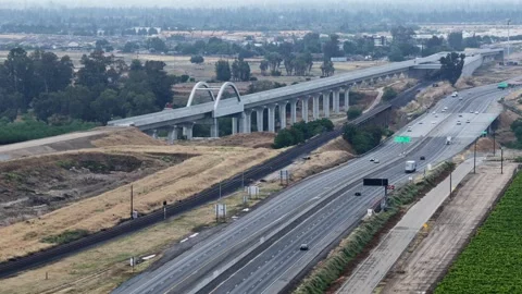 Arched viaduct curves above multi-lane highway, traffic streaming past green Stock Footage 337746350