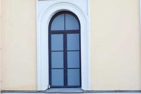 Arched window with black frame on beige building facade. 写真素材