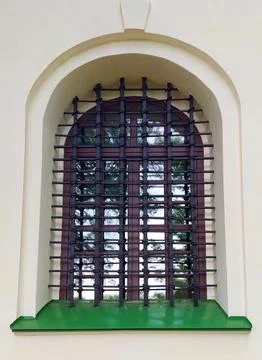 Arched window with forged iron security bars on white wall of ancient building Stock Photos