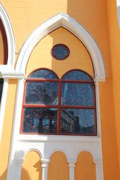 An arched window on the side of an orange and yellow church with colorful g.. Stock Photos