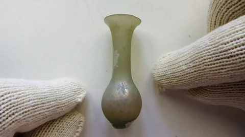 Archeologist inspects ancient small Roman glass scent bottle used for perfume Stock-Footage 79974739