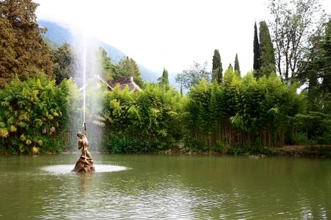 Archer fountain on lake with trees in green magic park. Stock Photos