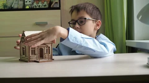 An architect boy collects a model of a house made of plywood. The boy talks Stock Footage 167796499
