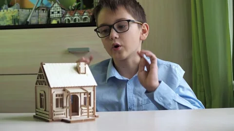 An architect boy collects a model of a house made of plywood. The boy talks Stock Footage 168372659