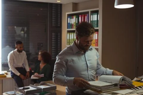 Architect checking file while colleagues interacting in background Stock Photos
