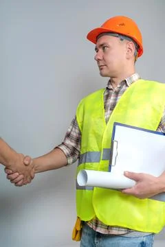 Architect-contractor, builder, worker, shakes hands with a client on a gray b Stock Photos