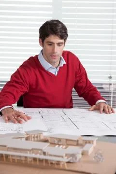Architect at desk looking at plans and building model Stock Photos